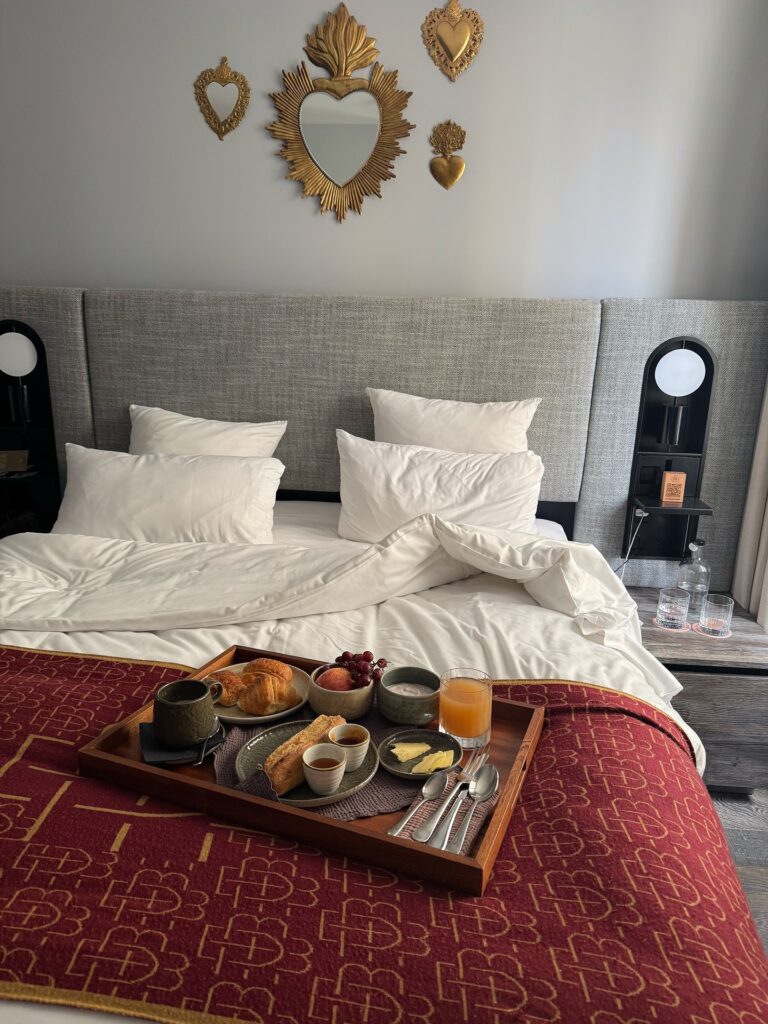 Plaid rouge à motif posé sur un lit avec petit déjeuner dans une chambre de l’hôtel Boudoir des Muses
