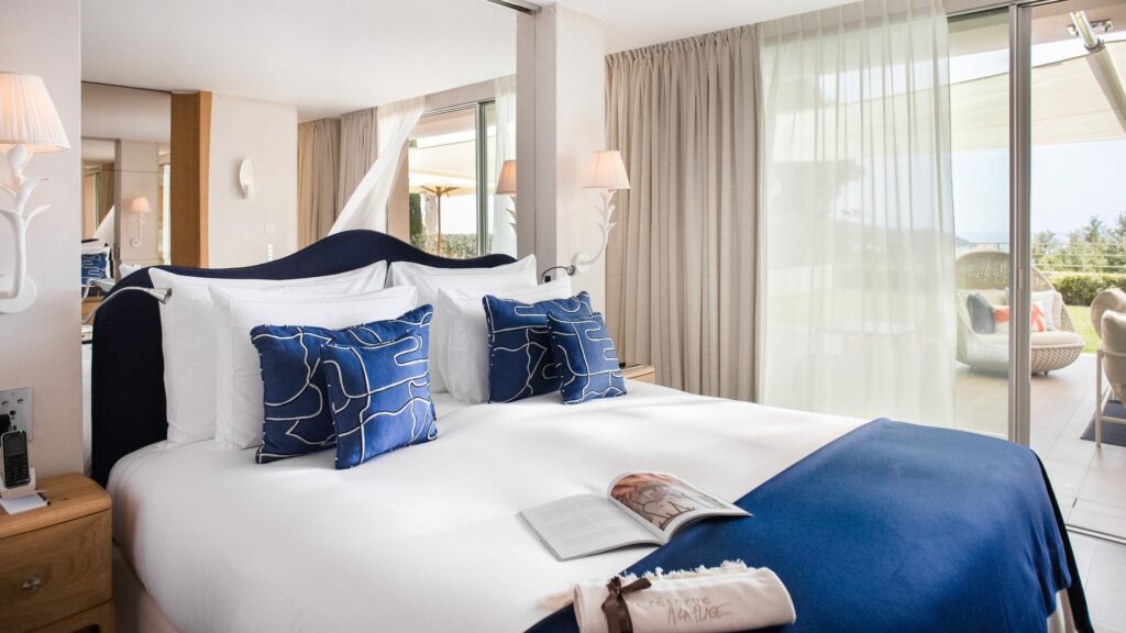 Chambre à La Réserve Ramatuelle avec lit double, coussins bleus et linge de lit haut de gamme
