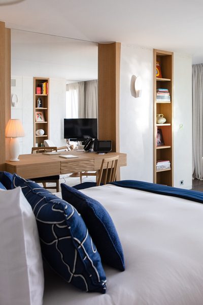 Chambre élégante à La Réserve Ramatuelle avec lit double, coussins bleus, plaid bleu et espace bureau en bois