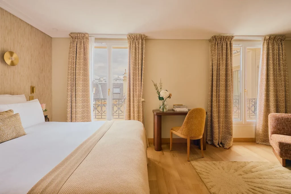 Plaid en maille beige disposé en bout de lit dans une chambre lumineuse avec vue extérieure