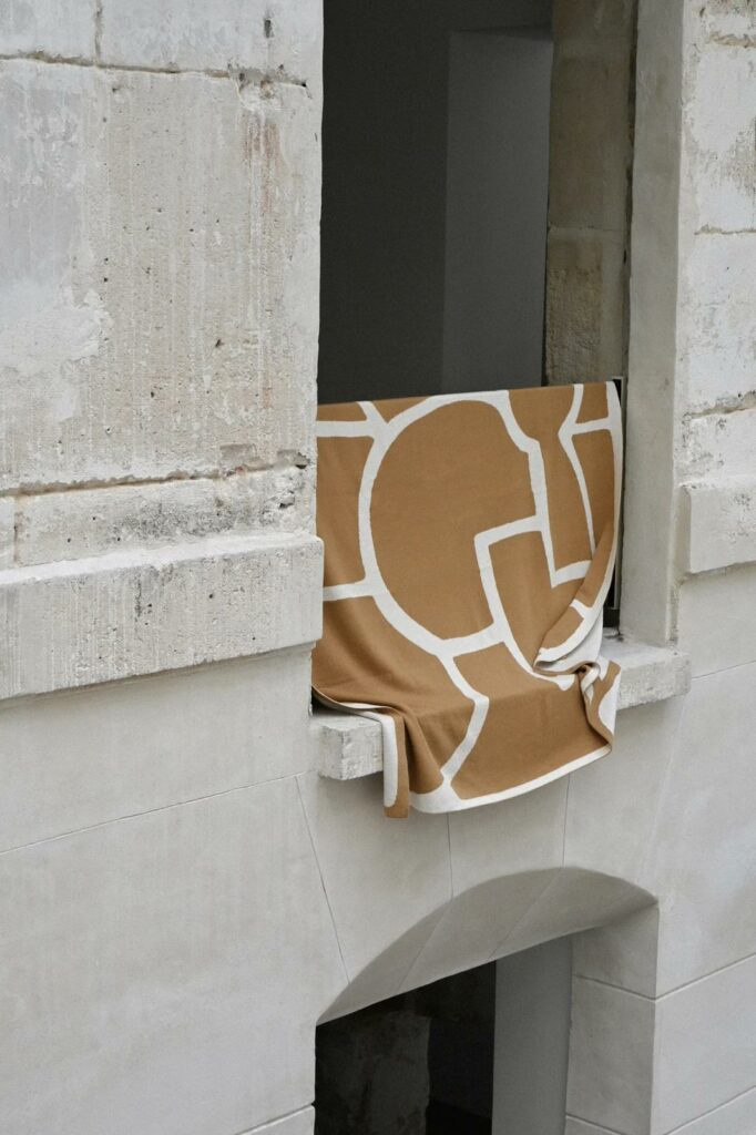 Plaid en maille bouclette avec motif géométrique posé sur un rebord en pierre, mise en scène textile contemporaine