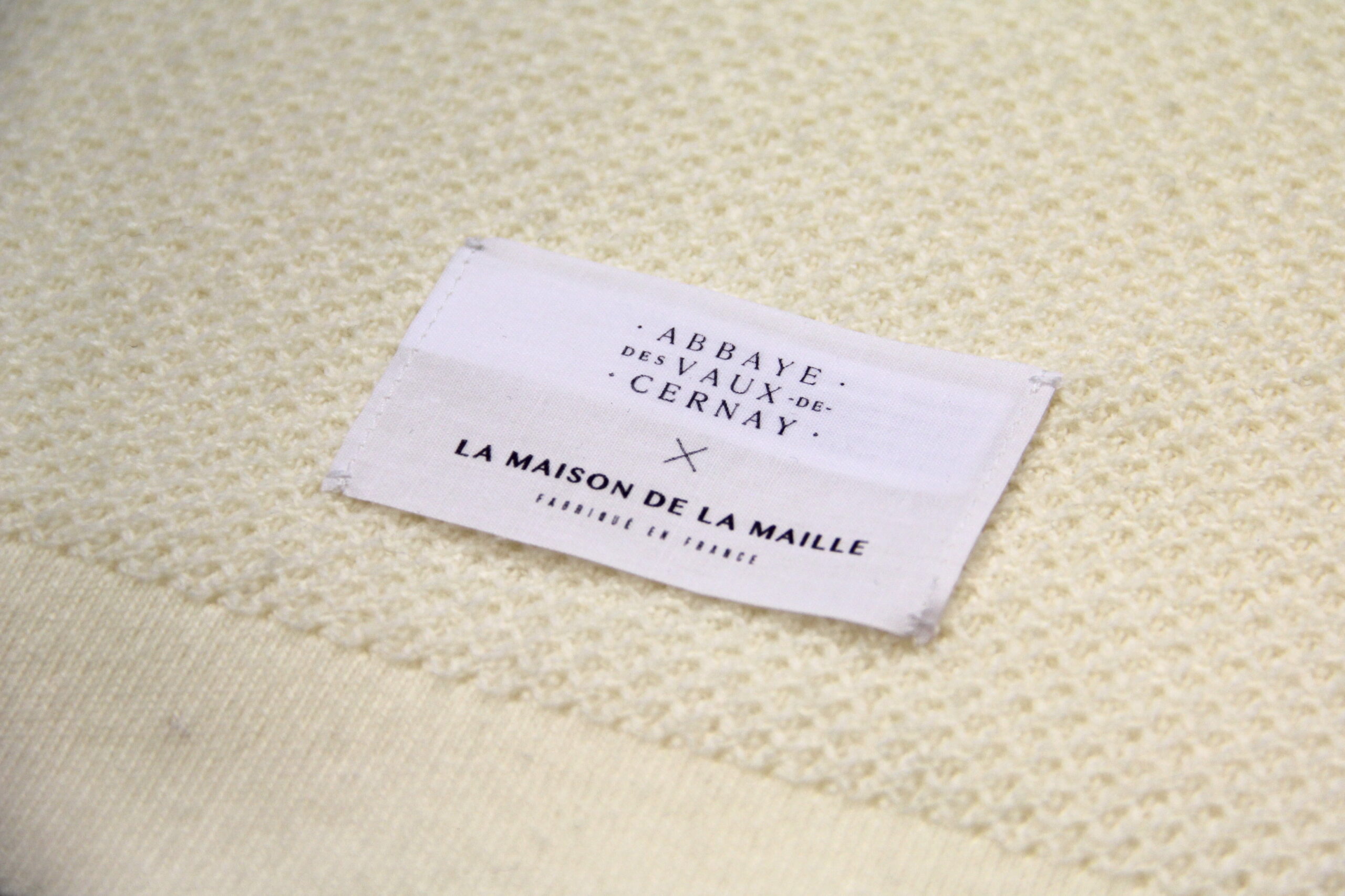 Étiquette La Maison de la Maille sur plaid en maille piquée, collaboration Abbaye des Vaux de Cernay, détail matière et finition