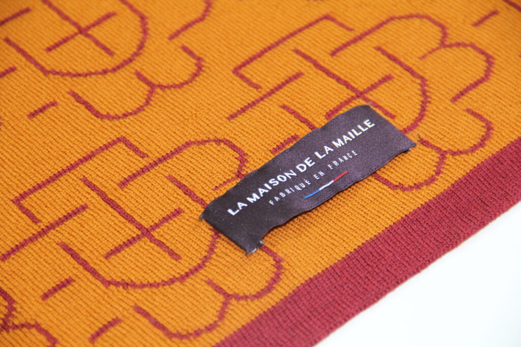 Gros plan sur l’étiquette La Maison de la Maille cousue sur un plaid en maille jaune et rouge