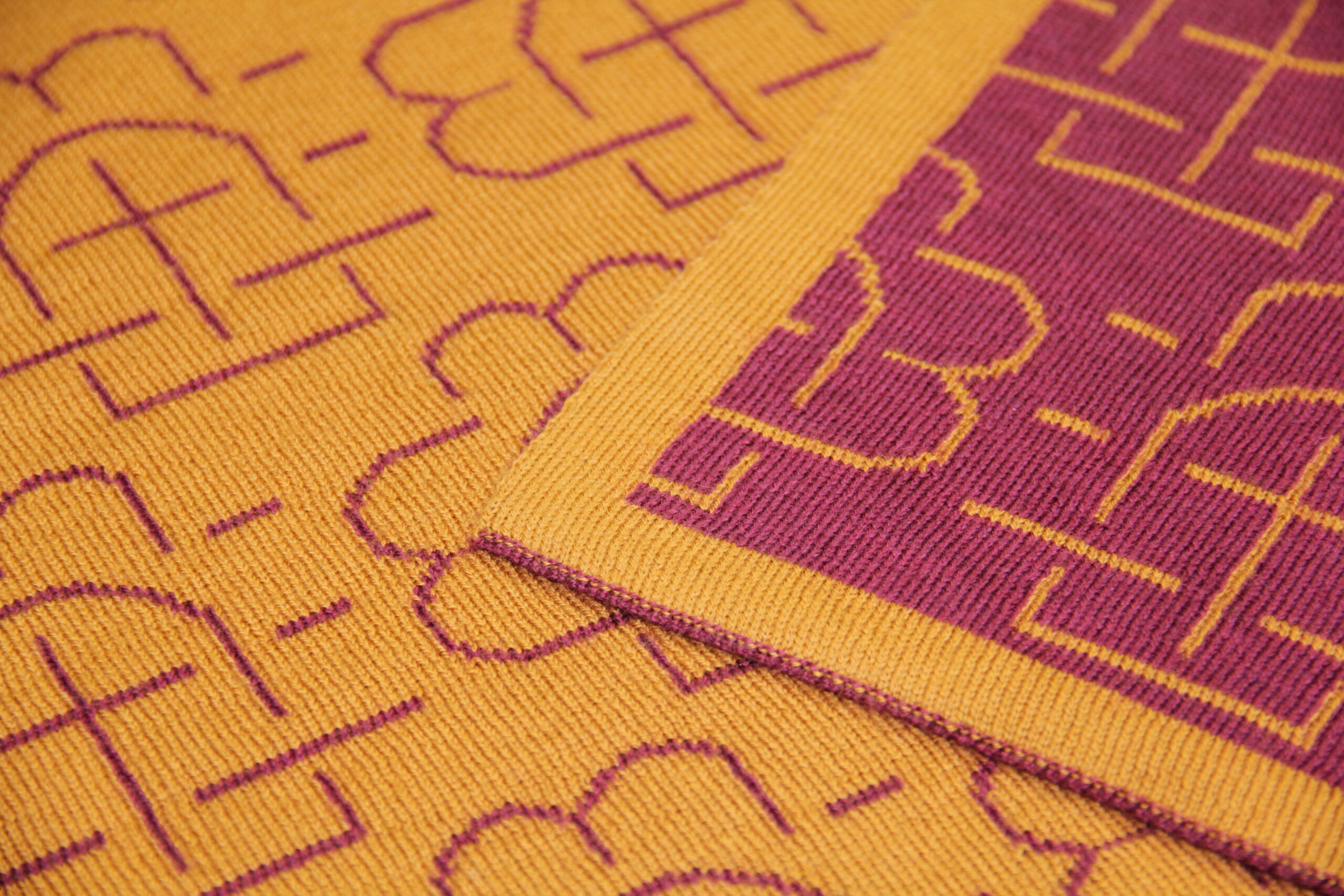 Détail de la maille d’un plaid en laine jaune et rouge avec motif graphique, réalisation La Maison de la Maille