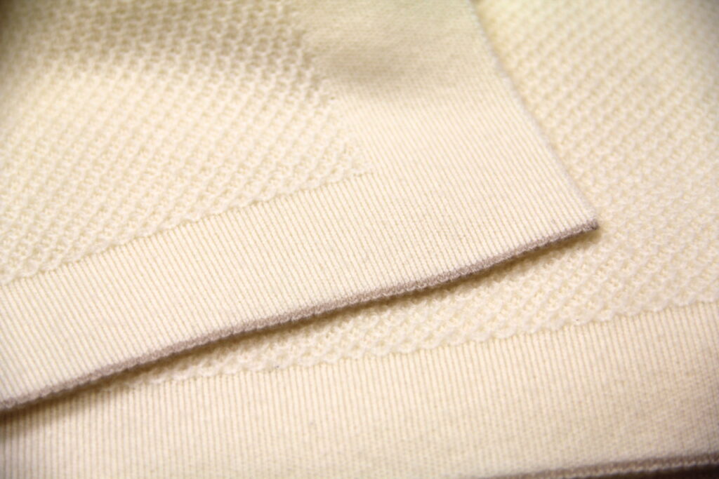 Gros plan sur la texture d’un plaid en maille écrue La Maison de la Maille, mettant en avant la finesse et le relief du tricot