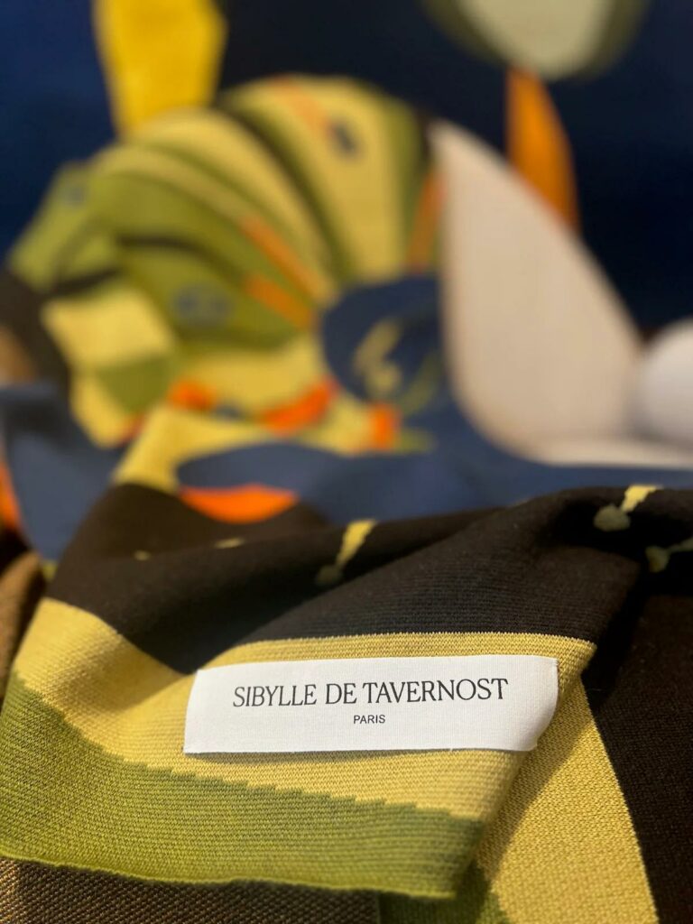 Détail d’un plaid en maille avec motif graphique et étiquette Sibylle de Tavernost, textile haut de gamme