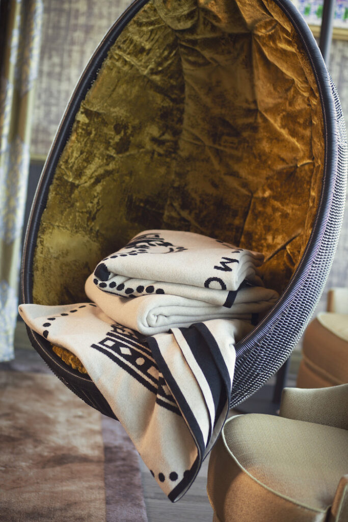 Plaids en cachemire recyclé Moët & Chandon empilés dans un fauteuil design, mise en scène textile haut de gamme