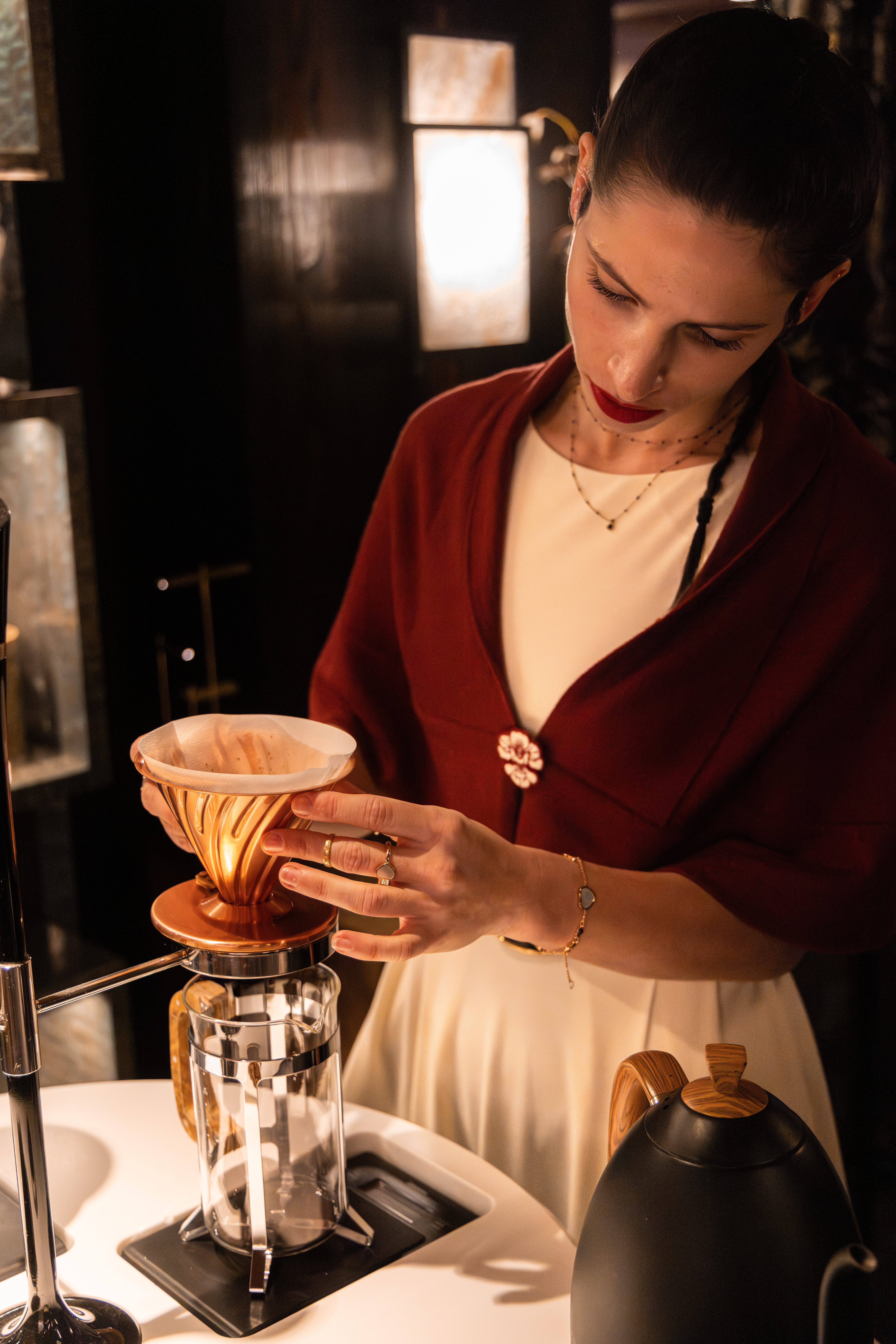 Serveuse préparant un café filtre portant une cape bordeaux sur mesure.