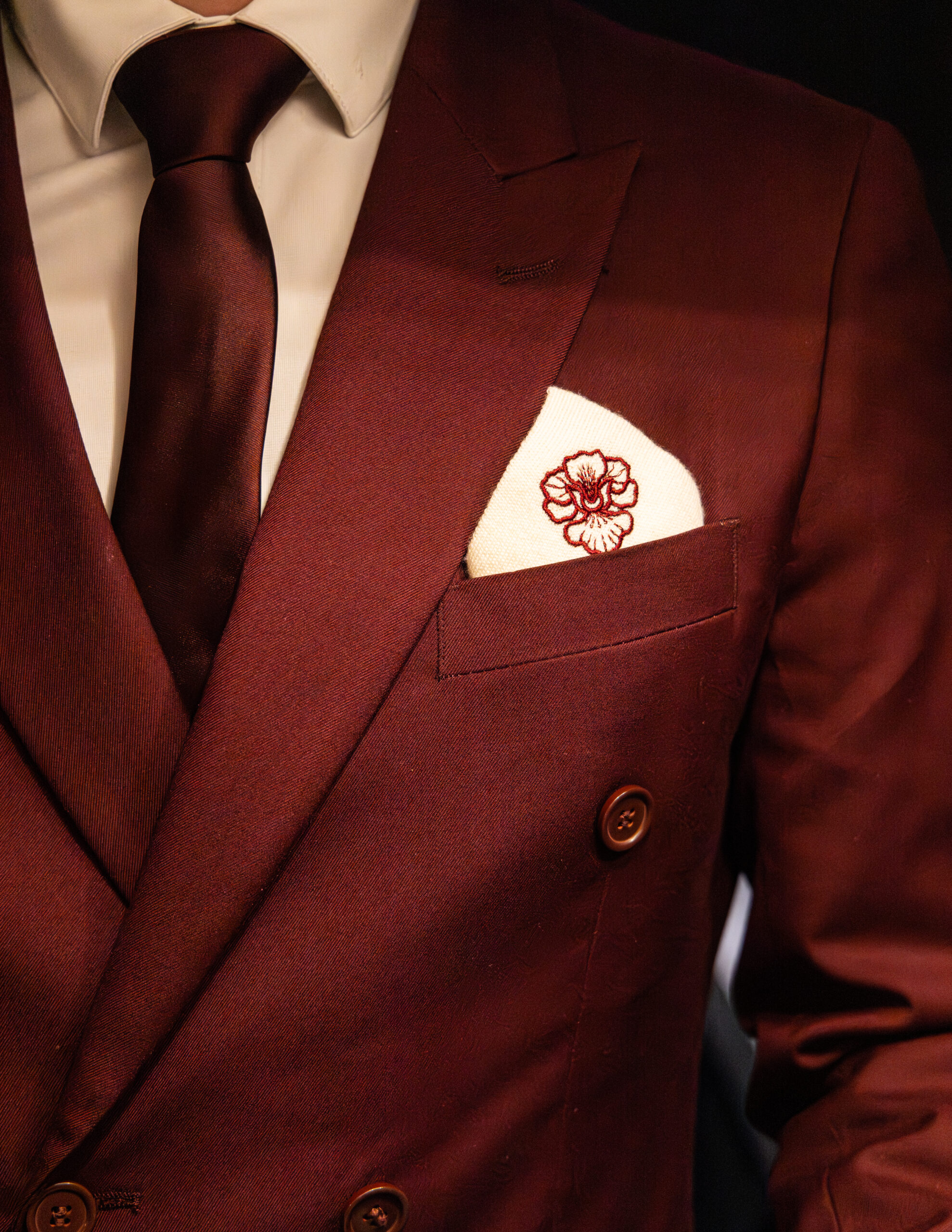 Détail d’un costume bordeaux avec pochette brodée florale personnalisée.