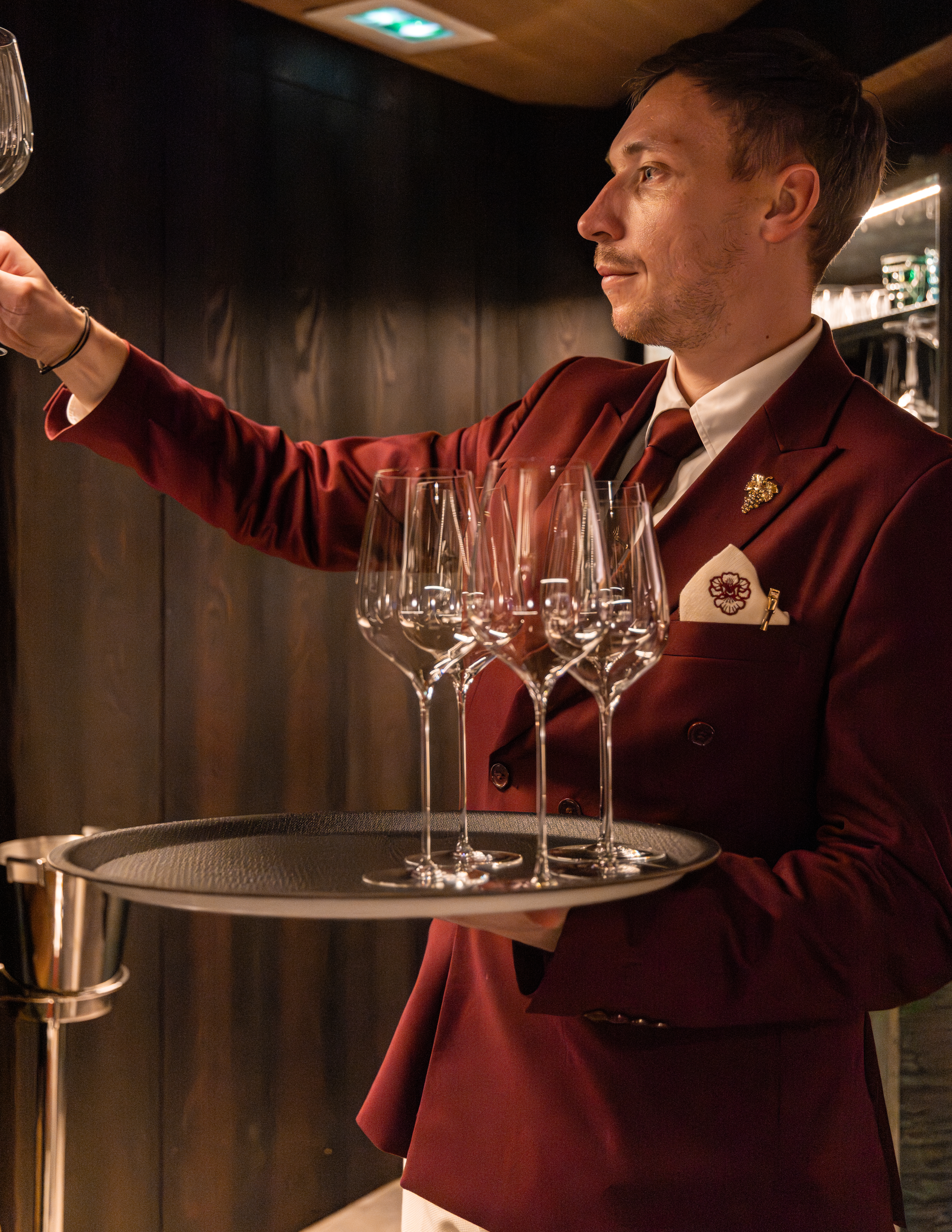 Serveur en costume bordeaux portant un plateau de verres à vin.